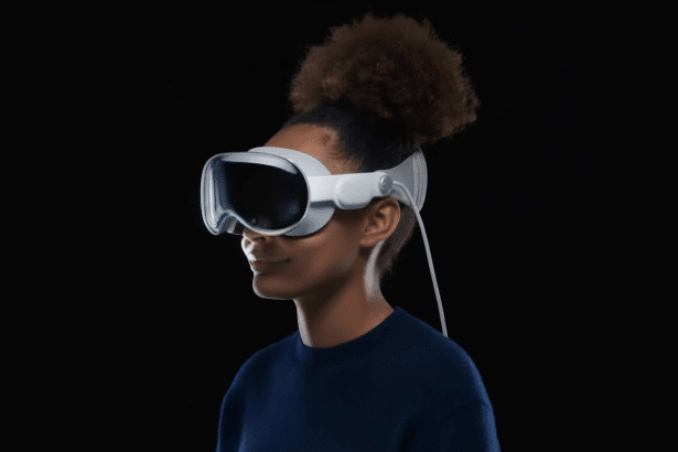 A person with dark, curly hair in a bun wearing white virtual reality goggles with a dark visor against a black background. Filename : personwith vrg oggles.png