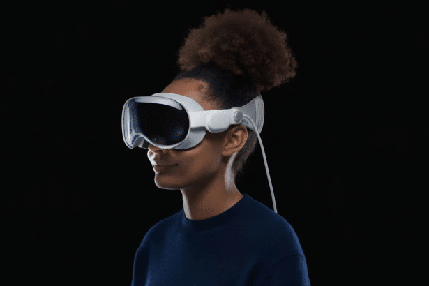 A person with dark skin and curly hair tied up , wearing a white virtual reality headset against a plain black background.