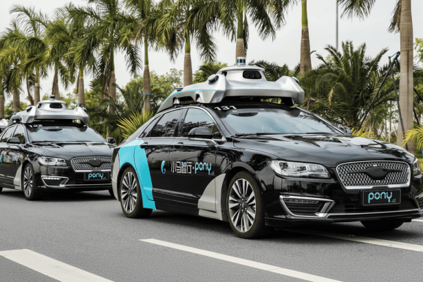 Three black Pony.ai autonomous vehicles with blue accents on the side are driving in a line on a paved road lined with palm trees.