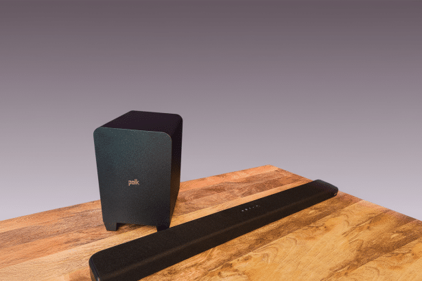 A professional shot of a Polk soundbar and subwoofer on a wooden table . The background is a soft , professional grey gradient. Filename : polk soundbarsub wooferprofessional . png