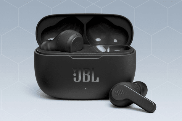 A pair of black JBL earbuds in an open charging case, with one earbud removed and placed beside the case, all set against a professional light grey background with a subtle geometric pattern. Filename : jbl earbuds1 69. png
