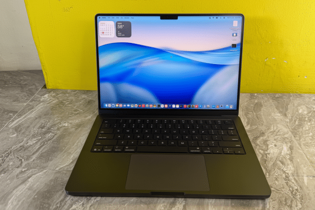 A professional shot of a modern black laptop with a vibrant blue and white wavy background on its screen, set against a yellow wall and a gray marbled surface .