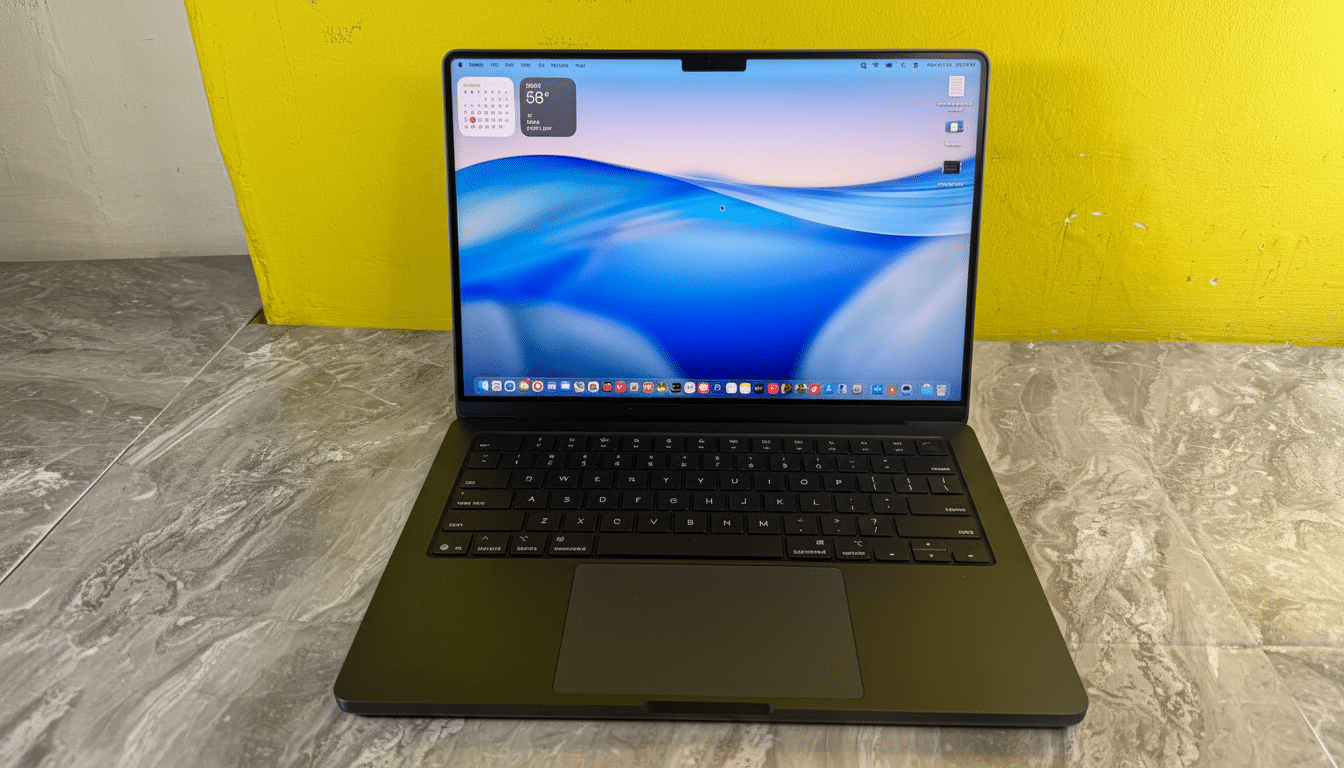 A professional shot of a modern black laptop with a vibrant blue and white wavy background on its screen, set against a yellow wall and a gray marbled surface .