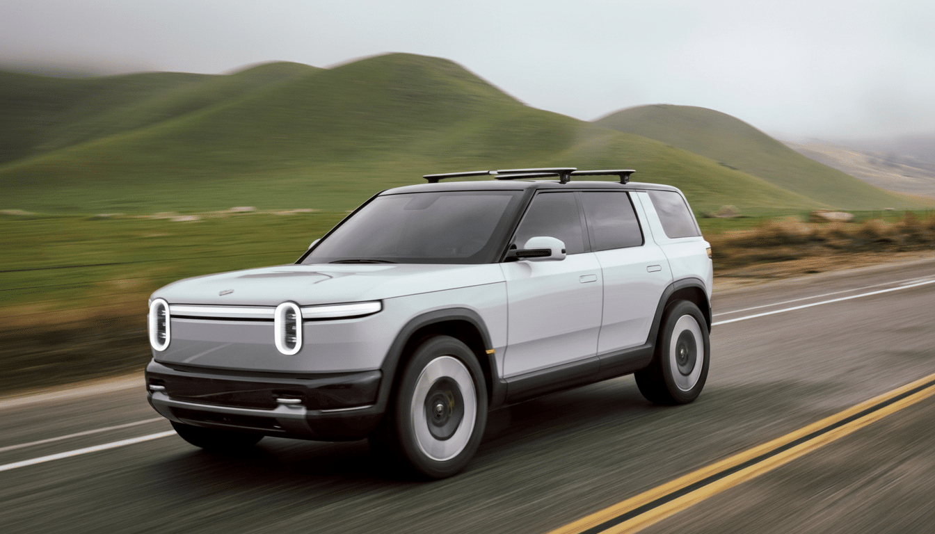 A professional shot of a light grey Rivian R 1S SUV driving on a road with green hills in the background, resized to a 16: 9 aspect ratio.