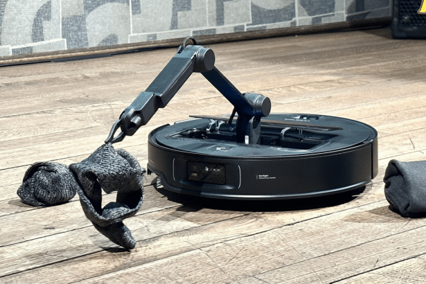 A professional shot of a robotic arm attached to a circular base , holding a crumpled grey cloth, on a wooden floor.