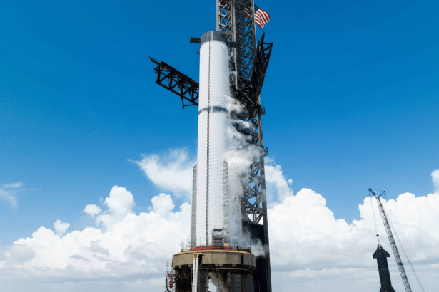 A large white rocket on a launchpad under a blue sky with white clouds, with the American flag visible at the top.