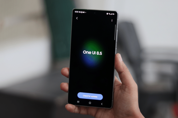Hand holding a smartphone displaying One UI 8.5 on a dark screen with a Check for updates button.