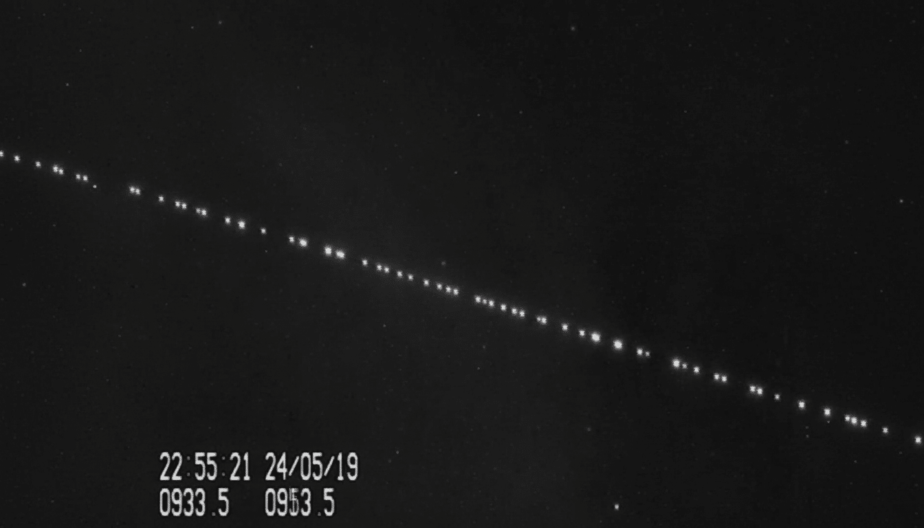 A black and white image showing a diagonal line of bright dots , likely satellites , against a dark starry sky. There is a timestamp and other data in the bottom left corner.
