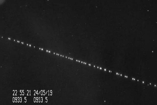 A black and white image showing a diagonal line of bright dots , likely satellites , against a dark starry background , with a timestamp and numerical data in the bottom left corner .