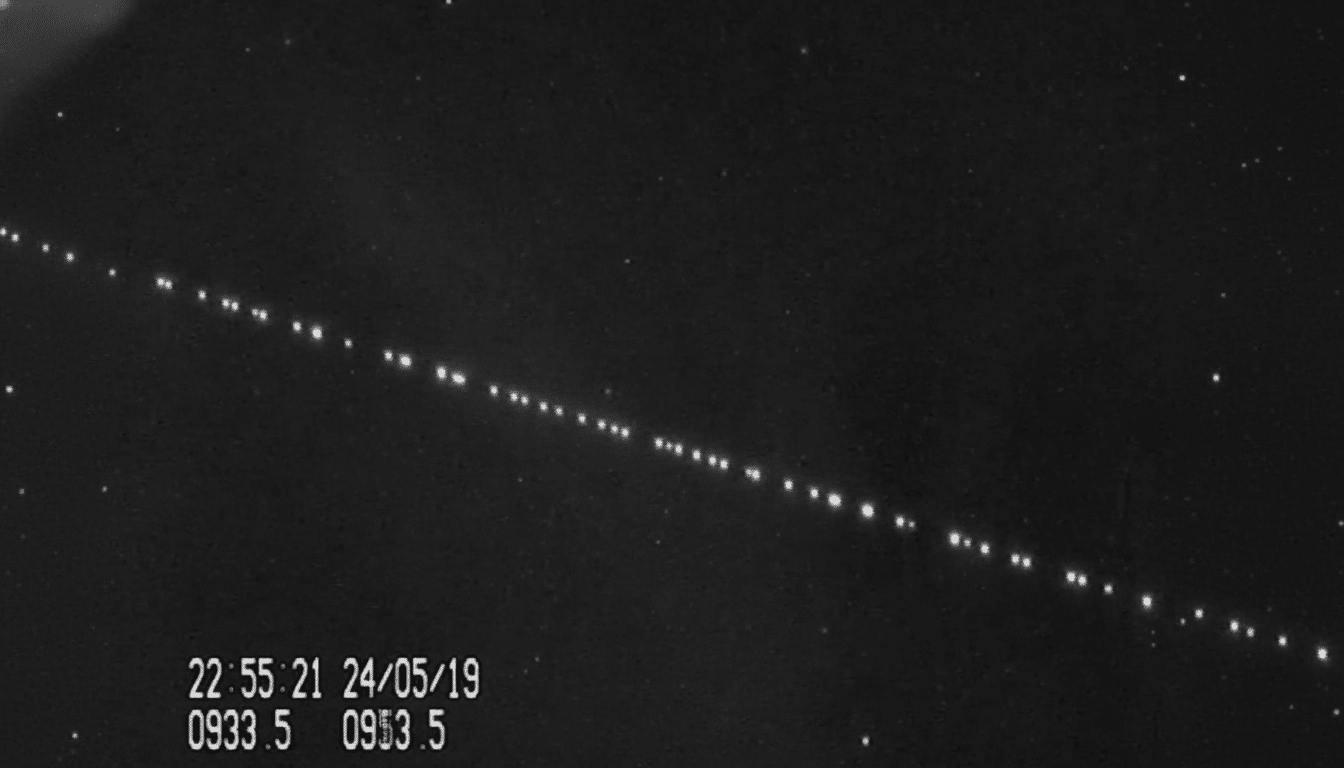 A black and white image showing a diagonal line of bright dots , likely satellites , against a dark starry background , with a timestamp and numerical data in the bottom left corner .