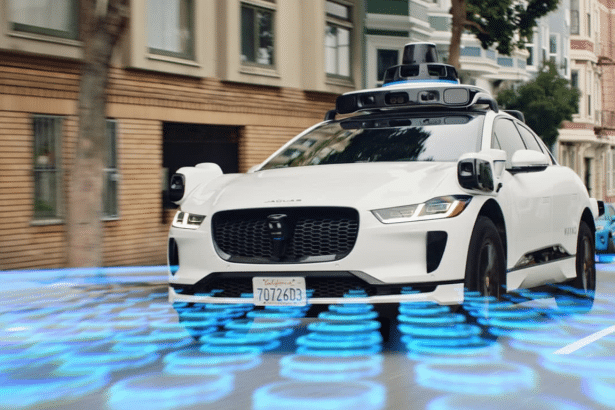 A white self -driving Jaguar I -Pace with advanced sensors on its roof and sides , driving on a city street with blue glowing digital patterns emanating from beneath it, indicating its autonomous operation.
