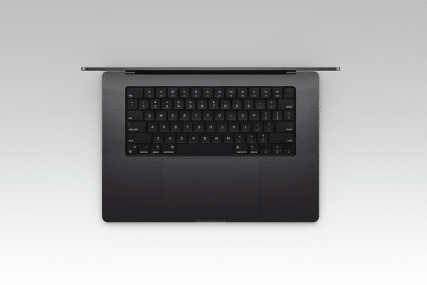 An overhead view of a dark gray laptop with a keyboard and trackpad, set against a soft, light gray gradient background .