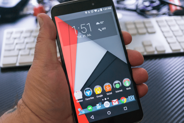 A hand holding a smartphone displaying the home screen with various app icons, resized to a 1 6: 9 aspect ratio.