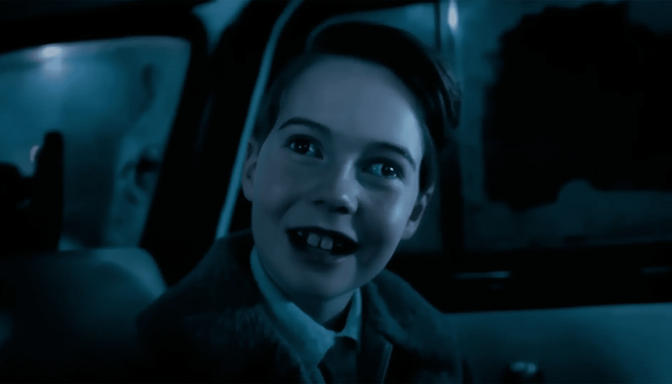 A young boy with dark hair and a suit smiles , looking upwards, in a dimly lit car interior. Filename : smiling boyin car.png