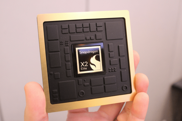 A hand holds a gold and black Snapdragon X2 Elite chip, with the logo visible in the center.
