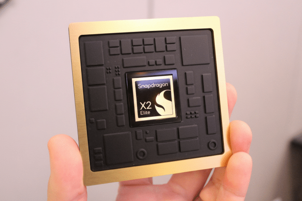 A hand holds a gold and black Snapdragon X2 Elite chip, presented professionally .