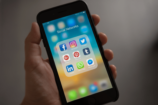A hand holding a smartphone displaying a Social Networks folder with various social media app icons.