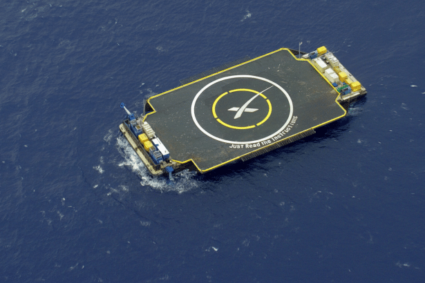 An aerial view of the Just Read the Instructions drone ship with a SpaceX logo on its hel ipad, floating in the ocean.