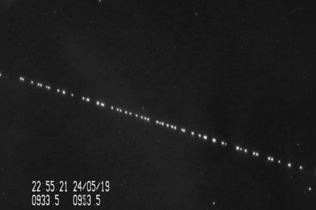 A dark , starry night sky with a diagonal line of bright, evenly spaced lights , likely a satellite constellation, and a timestamp in the bottom left corner .