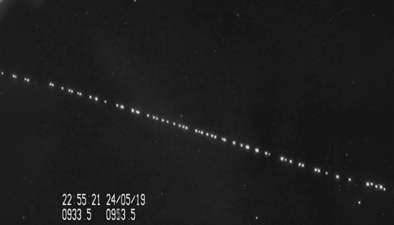 A dark , starry night sky with a diagonal line of bright, evenly spaced lights , likely a satellite constellation, and a timestamp in the bottom left corner .