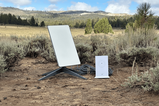 A Star link satellite dish and a calibration target on a stand are set up outdoors in a natural, open landscape with brush, trees, and hills under a p