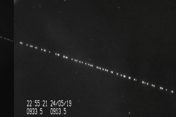 A professional, enhanced black and white image displaying a diagonal line of bright, evenly spaced dots against a dark background, representing a sate