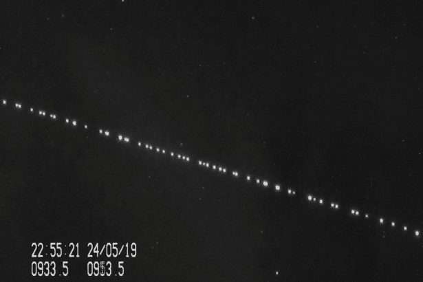 A dark, grainy image showing a diagonal line of bright, evenly spaced dots against a black background with a few scattered fainter dots. In the bottom