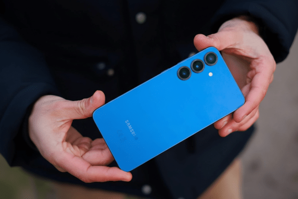 A person holding a blue Samsung smartphone with three camera lenses on the back.