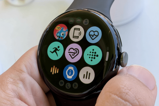 A close -up shot of a Google Pixel Watch being held, displaying various colorful app icons on its circular screen, including icons for fitness, heart rate, and notifications .