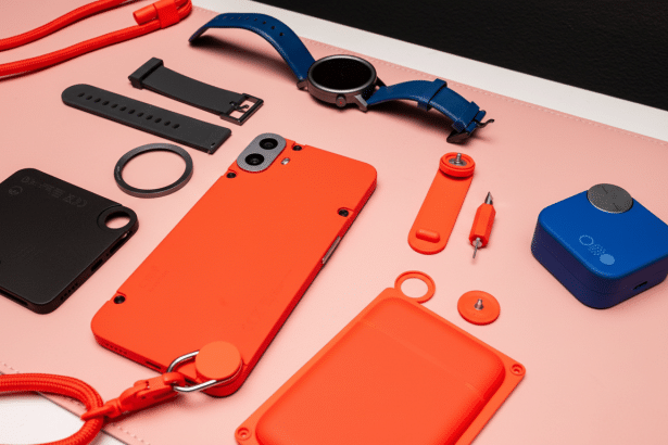 A flat lay of various tech accessories including a blue smartwatch, an orange smartphone case, a black phone case, and other small orange and black gadgets, all arranged on a light pink surface with a black background.