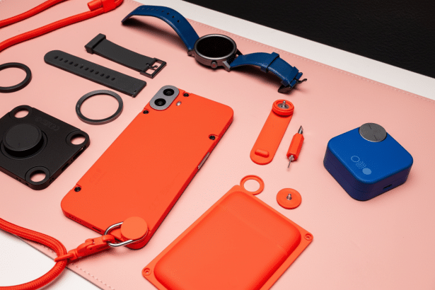 An array of tech accessories including an orange phone case, a blue smartwatch, and various tools and straps, laid out on a pink mat with a black and white background.