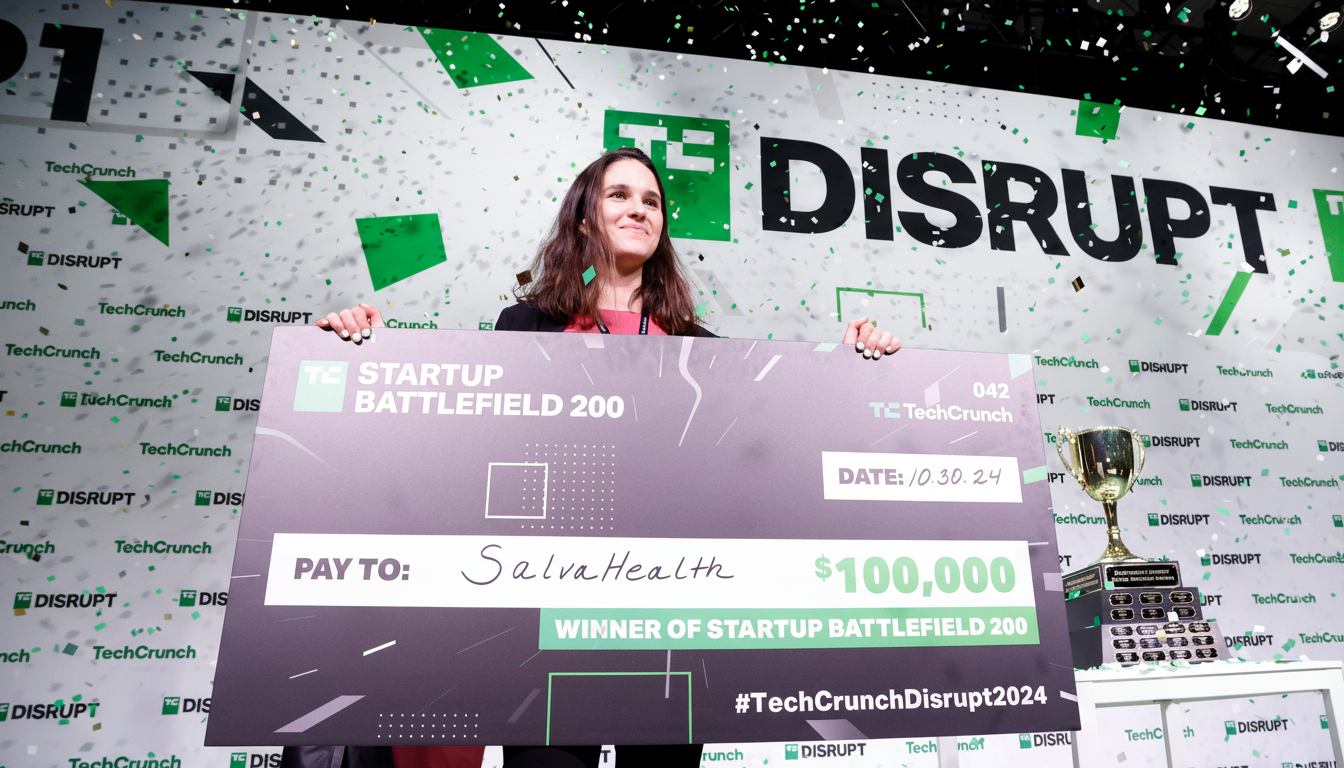 A woman holding a large check for $100,000 from TechCrunch Disrupt 2024, with confetti falling around her.