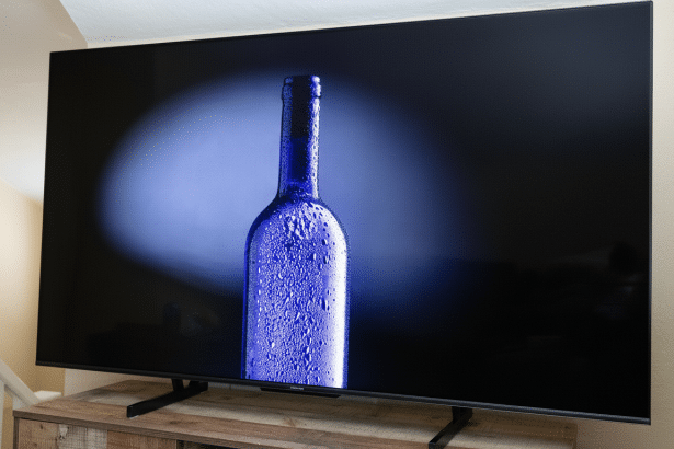 A modern television displaying a close -up image of a cold, condensation -covered blue bottle with a spotlight effect on a dark background.