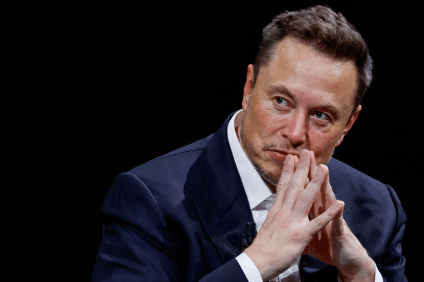A professional head shot of Elon Musk looking thoughtfully to the side, with his hands clasped under his chin against a dark background.
