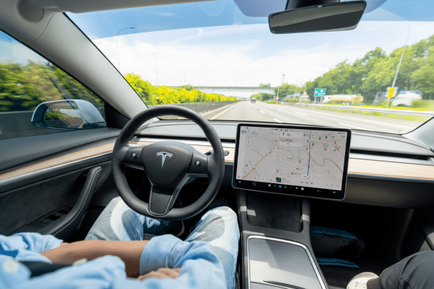 A person driving a Tesla car on a highway, with the steering wheel and the central display showing a navigation map visible .