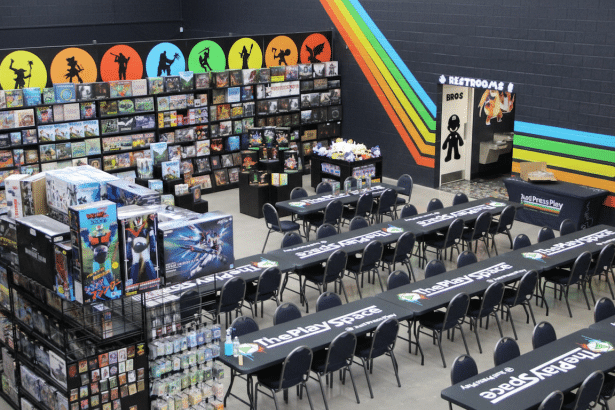 An overhead view of The Play Space, a game store and event venue, with long tables and chairs set up for gaming, shelves filled with board games, and various merchandise displays .