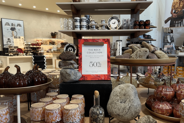 An in -store display of The Rock Collection with a 5 0% off sign , surrounded by other home goods and decorative items including candles and pumpkin -shaped glass.