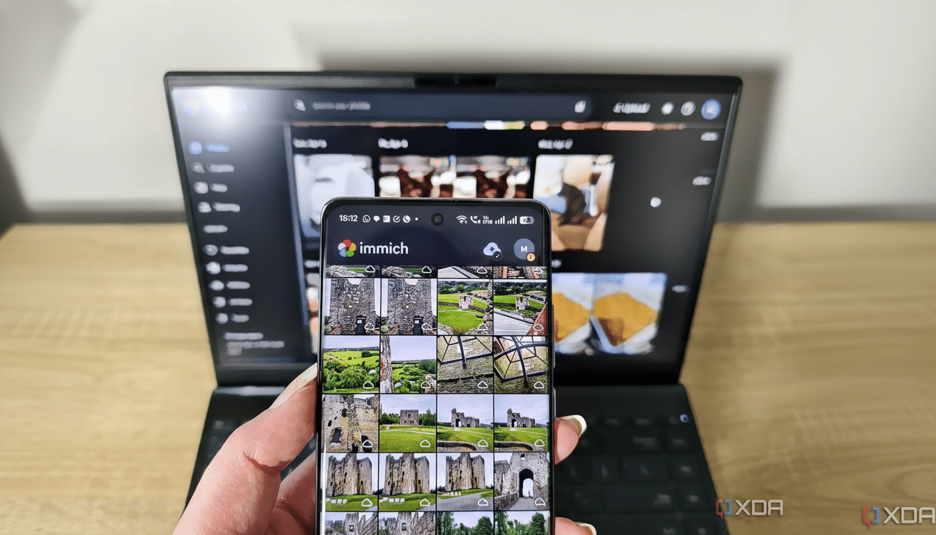 A hand holding a smartphone displaying the Immich app, with castle photos, in front of a laptop showing a web browser.
