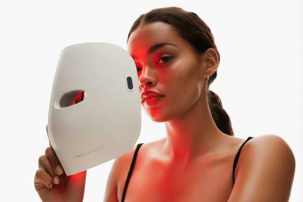 A woman holding a white facial mask device with red light glowing from it , against a white background.