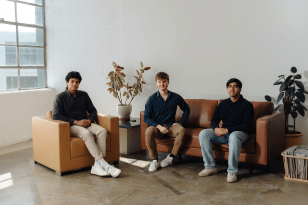 Three young men sit in an industrial -style room with a large window and potted plants, maintaining the original background.