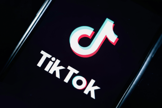 The TikTok logo and word mark displayed on a smartphone screen, with the iconic white, red, and blue musical note icon and white text on a black backg