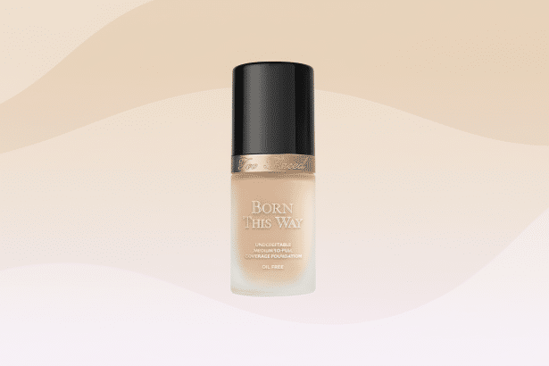 Too Faced Born This Way foundation bottle with a black cap and light beige liquid , centered on a light peach background with subtle, soft wavy patterns.