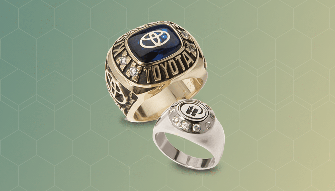 Two professional rings, one gold with a blue gem and Toyota logo, and one silver with a black and white emblem, displayed on a soft gradient backgroun