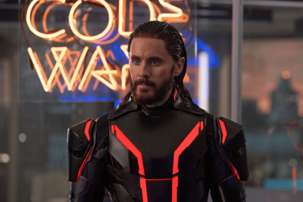 Jared Let o as Morbius in a black and red suit, looking thoughtfully with a neon sign in the background.
