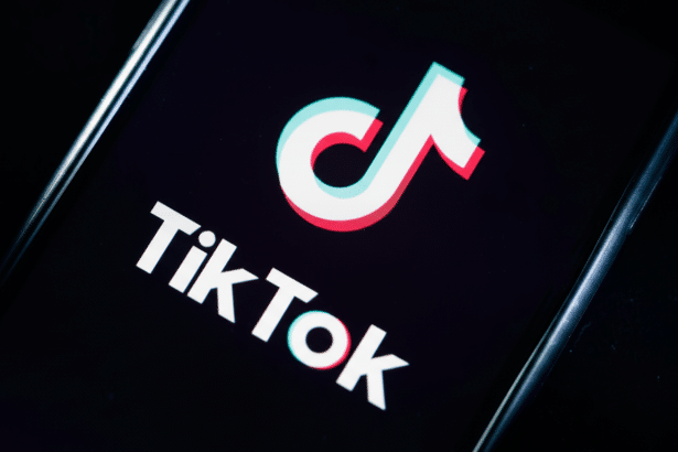 The TikTok logo displayed on a smartphone screen, featuring the iconic white musical note icon with blue and red outlines , and the TikTok word mark in white against a dark background, resized to a 16: 9 aspect ratio.