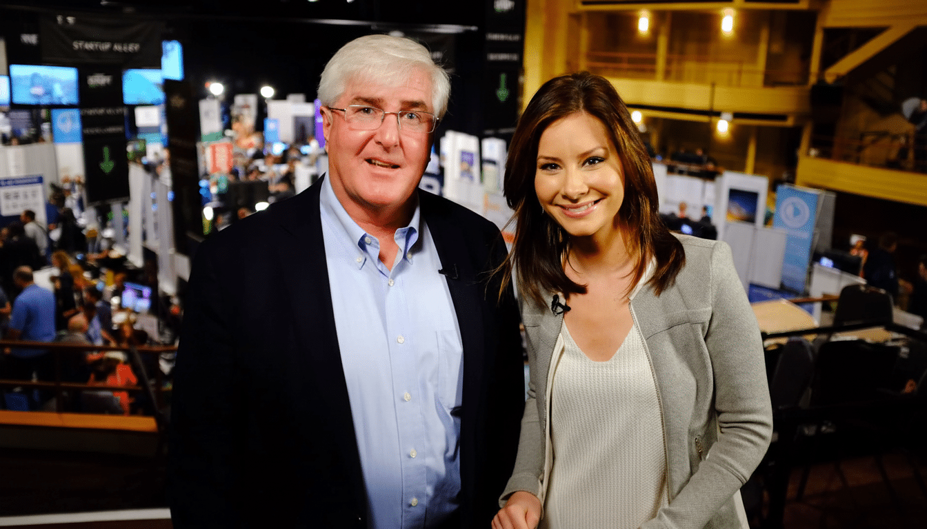 A man and a woman smiling at the camera, with a blurred background of a busy event or conference .