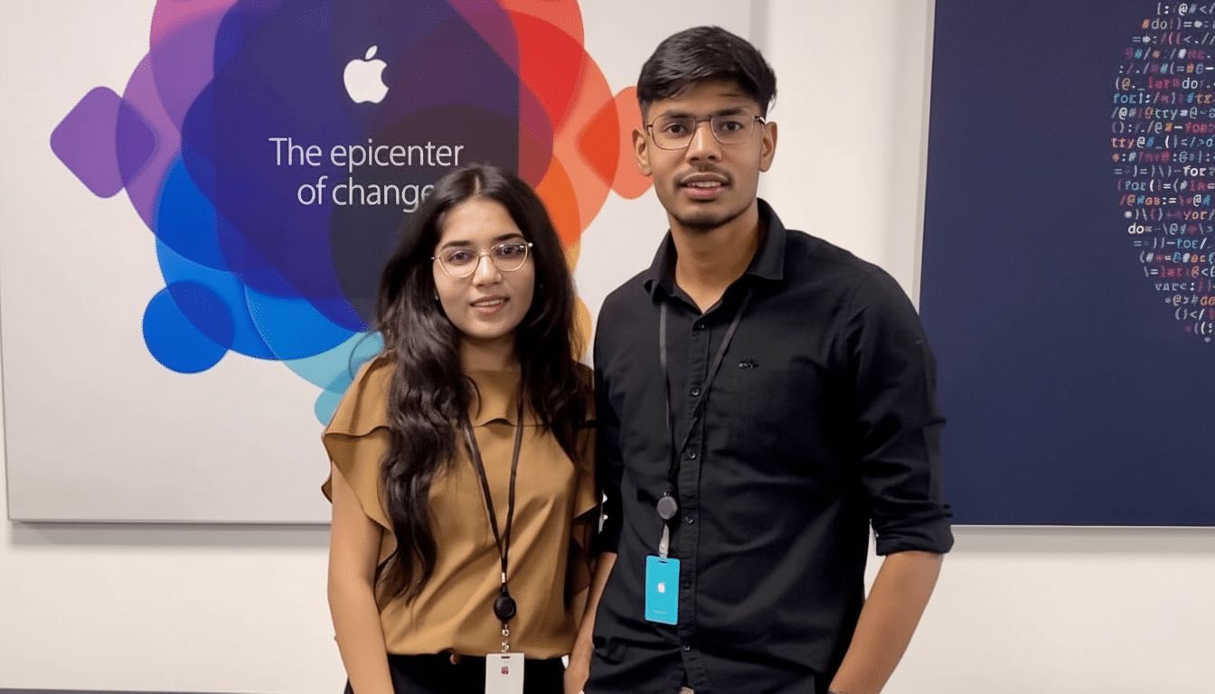 Two young professionals, a woman and a man, standing in front of a wall with an Apple logo and The epicenter of change text, along with coding script.
