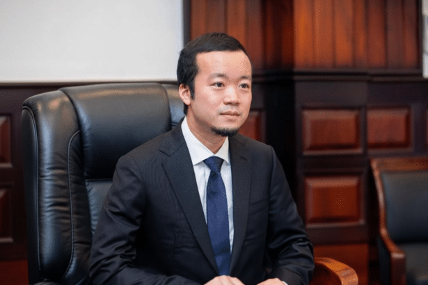A professional image of a man in a suit and tie sitting in a black leather chair , resized to a 16: 9 aspect ratio with the original background maintained .