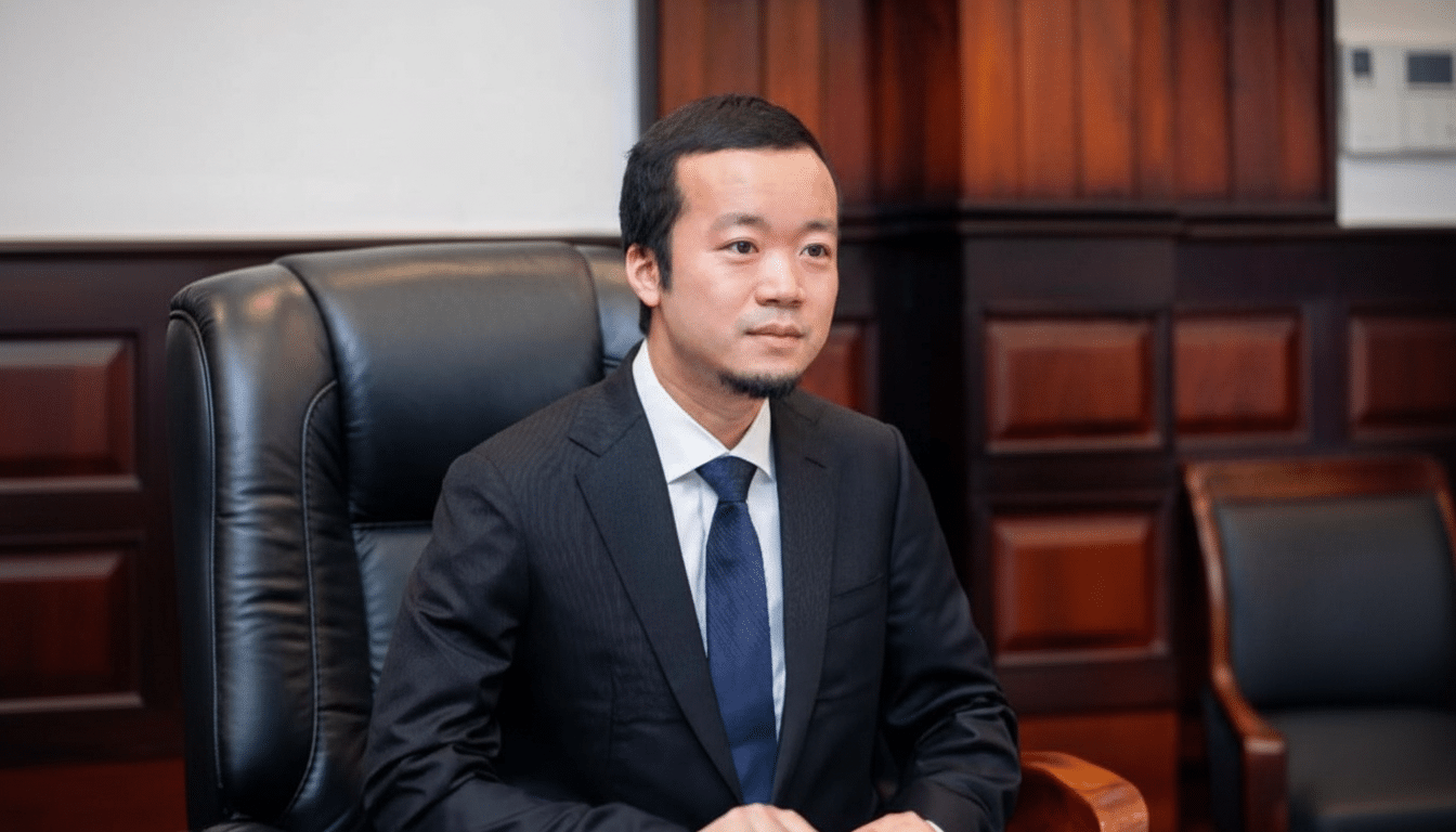 A professional image of a man in a suit and tie sitting in a black leather chair , resized to a 16: 9 aspect ratio with the original background maintained .