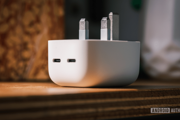 A white, rectangular charging adapter with two USB -C ports and two metal pr ongs for a UK socket, resting on a wooden surface.